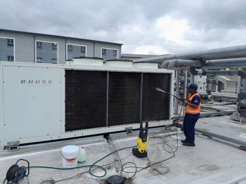 HVAC Technologies technician pressure-cleaning a rooftop chiller coil