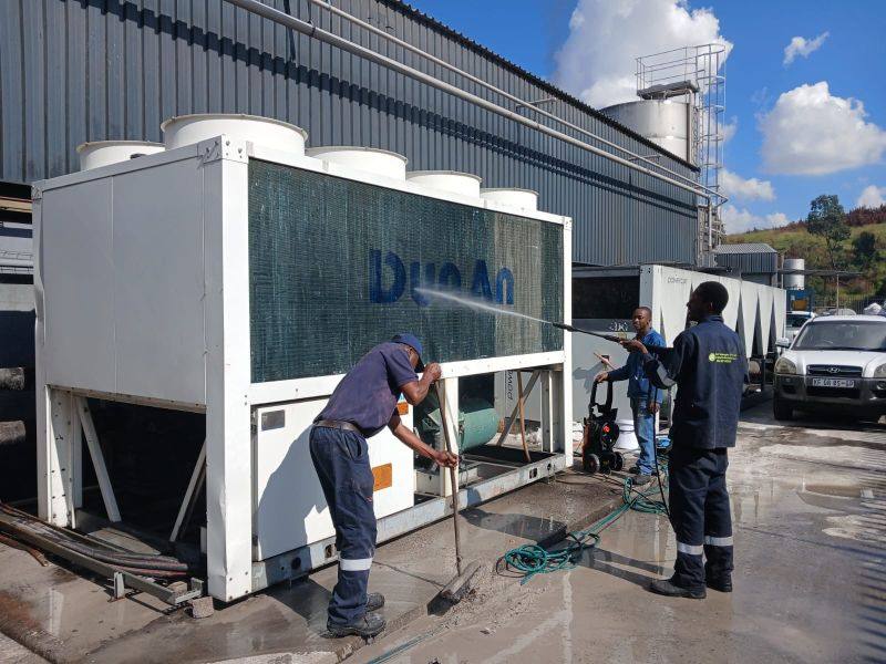 Technicians pressure-washing an air-cooled chiller coil